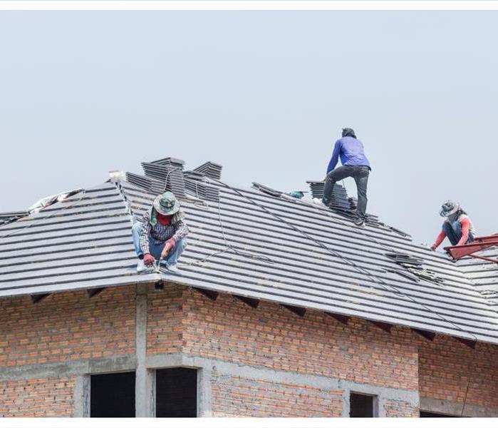 Workers installing concrete tiles on the roof while roofing house in construction site